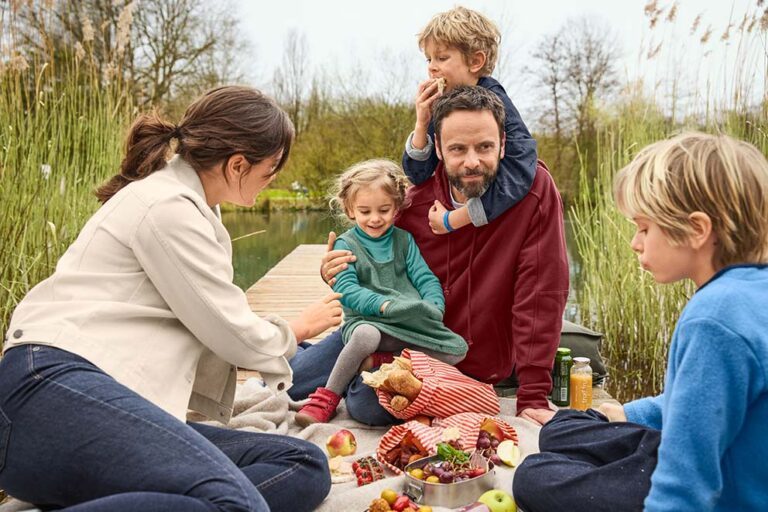 Eine Familie sitzt beim gemeinsamen Picknik an einem Steg am See.